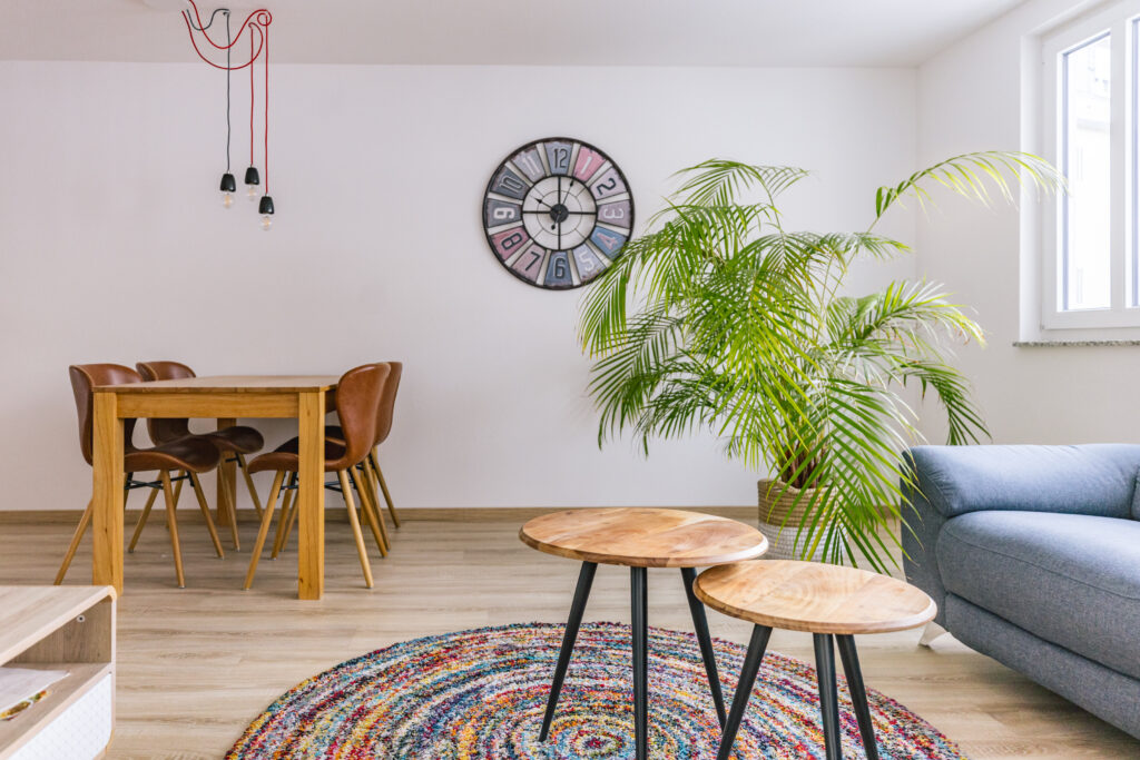 Heller Wohnraum mit Esstisch, Zimmerpalme, Wanduhr und blauem Sofa