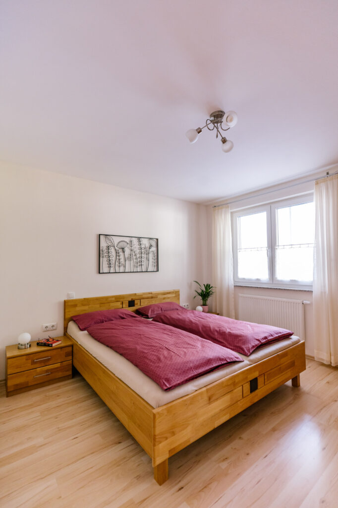 Schlafzimmer der Ferienwohnung Alte Pfarrgasse 5 mit Holz-Doppelbett, beerenfarbener Bettwäsche und Fenster