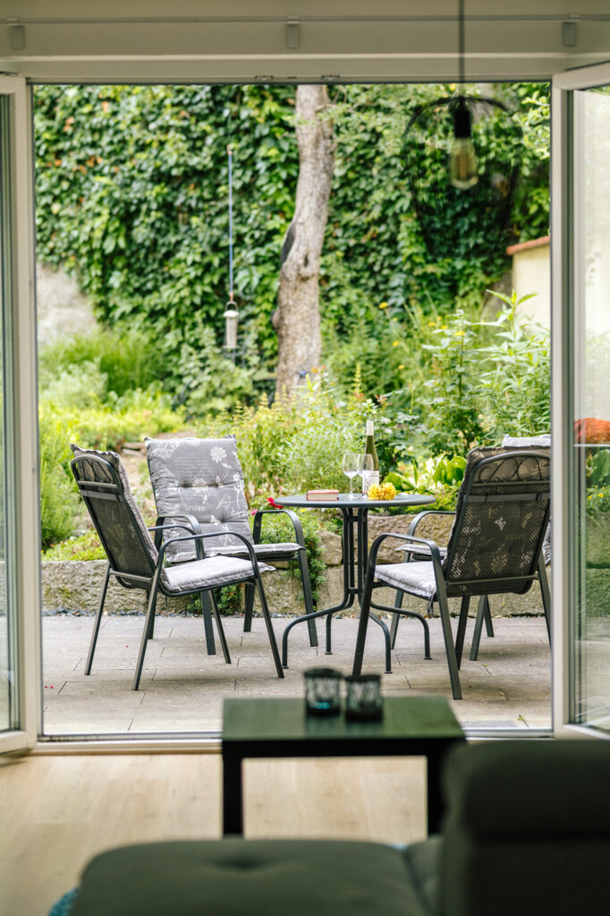 Blick durch die offene Terrassentür der Ferienwohnung Alte Pfarrgasse 5 auf Gartenmöbel im begrünten Innenhof