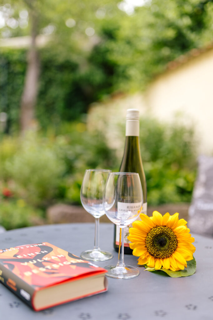 Weißwein mit zwei Gläsern, Buch und Sonnenblume auf dem Terrassentisch der Ferienwohnung Alte Pfarrgasse 5