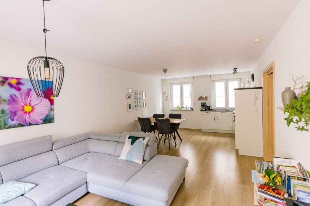 Offener Wohnraum der Ferienwohnung Alte Pfarrgasse 5 mit grauem Ecksofa, Esstisch und Blick zur Küche