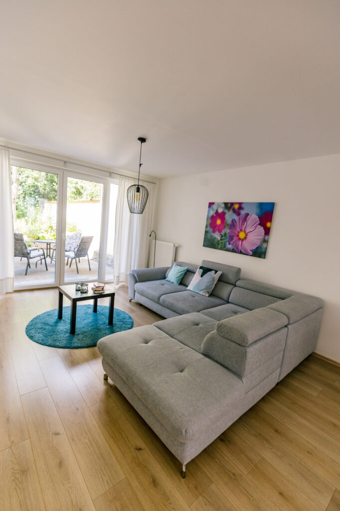 Wohnzimmer der Ferienwohnung Alte Pfarrgasse 5 mit grauem Ecksofa und bodentiefer Terrassentür zum Innenhof