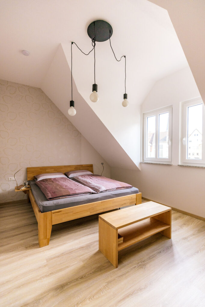 Gemütliches Schlafzimmer im Dachgeschoss mit Doppelbett aus Holz und stilvollen Pendelleuchten