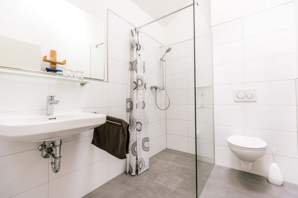 Modernes weißes Badezimmer mit begehbarer Dusche, Waschbecken und Wand-WC
